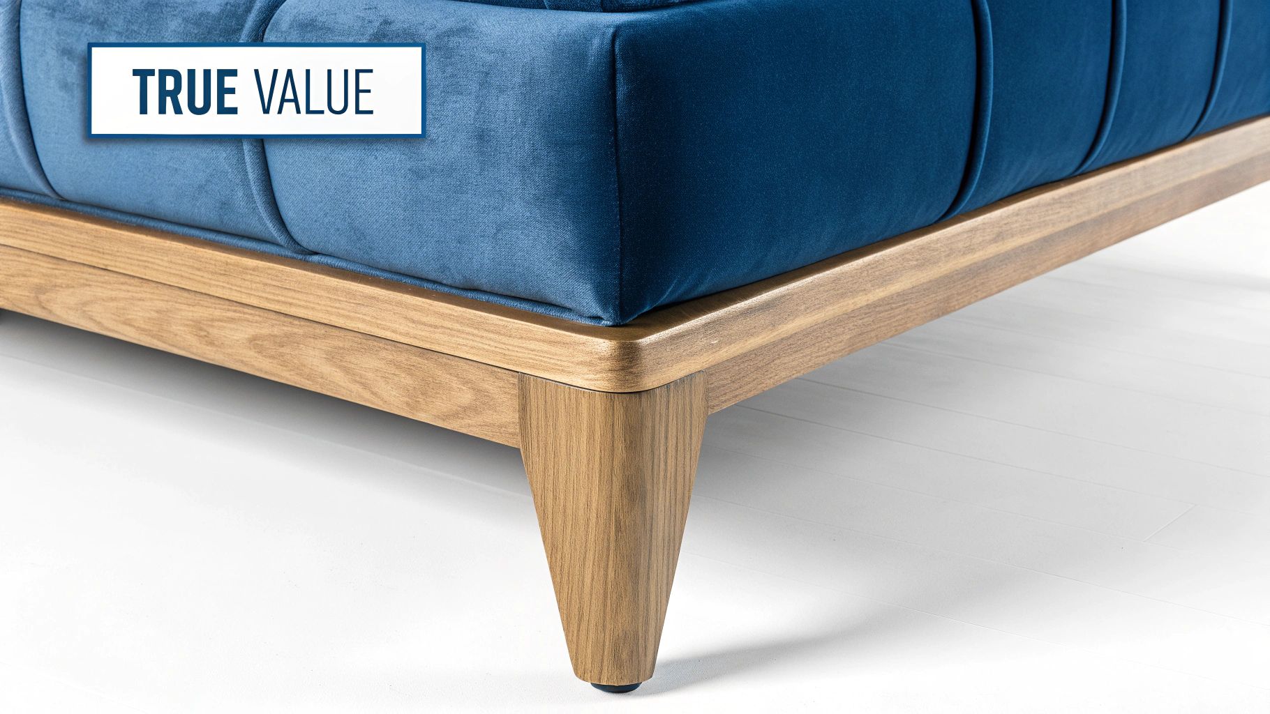 Close-up of a blue velvet sofa with a wooden base and tapered leg, featuring a 'TRUE VALUE' label.