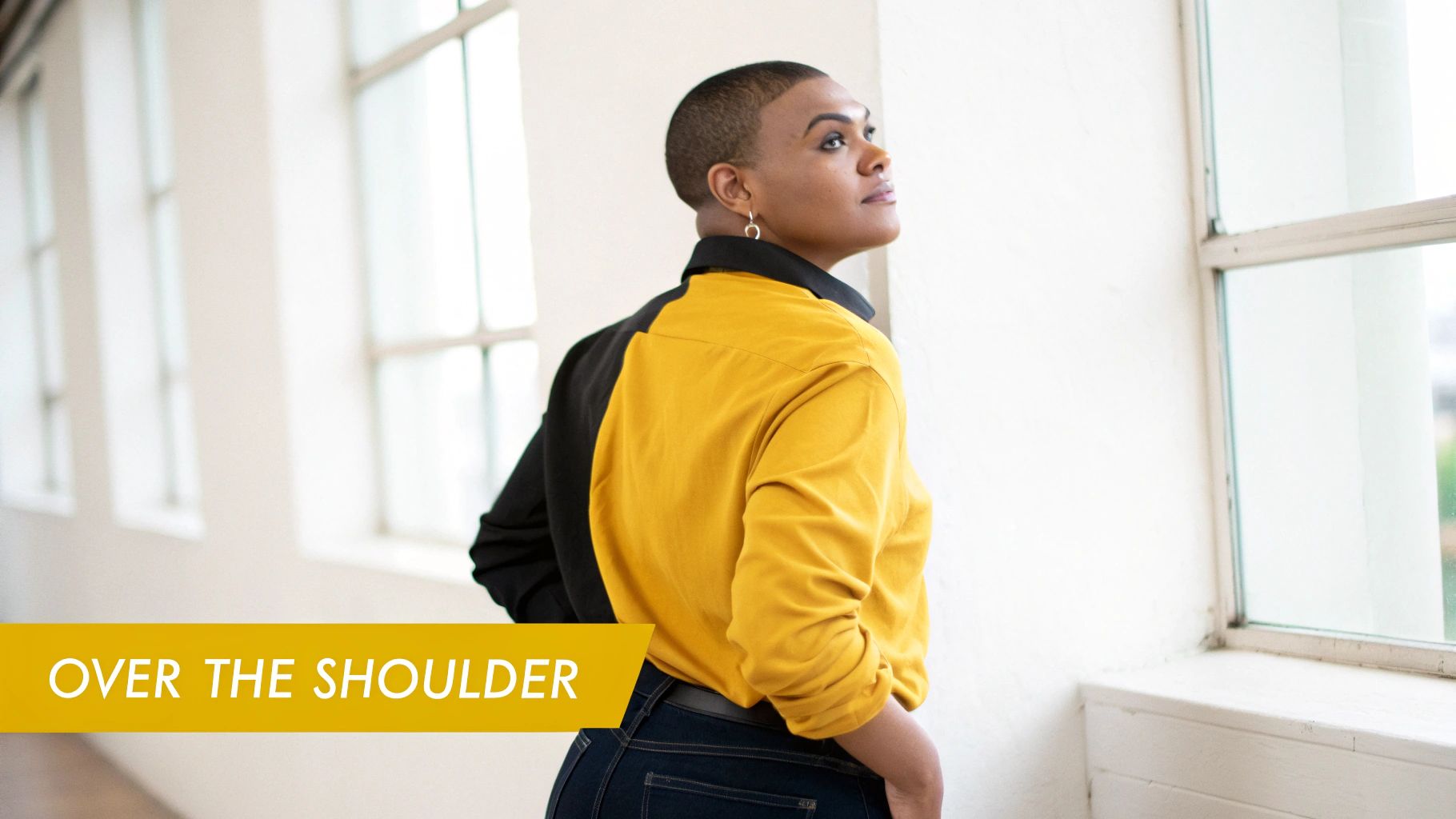 A person with a buzz cut, wearing a black and yellow shirt, looks out a window from an over-the-shoulder view.