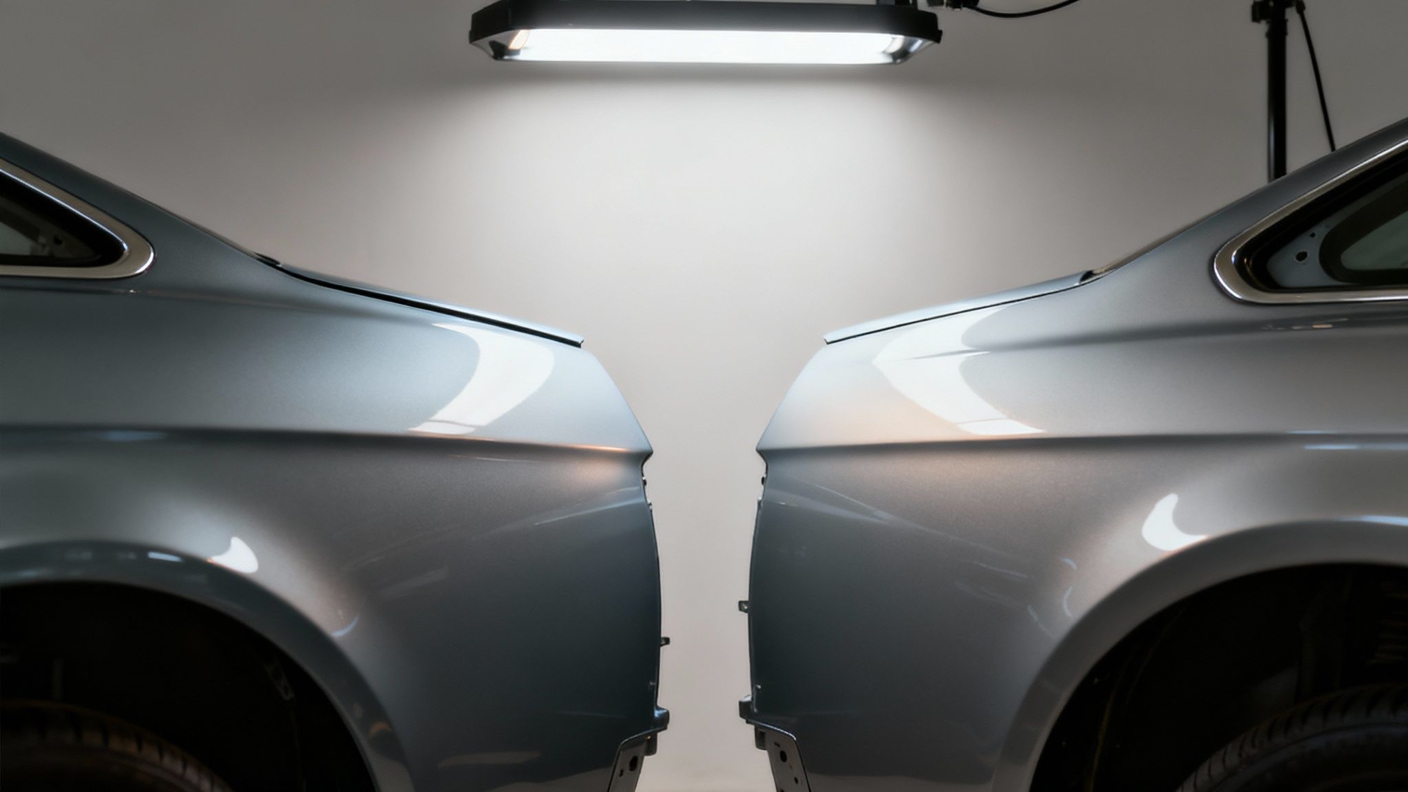 A mechanic pointing a torch at the chassis rail under the bonnet of a car, inspecting for signs of damage.