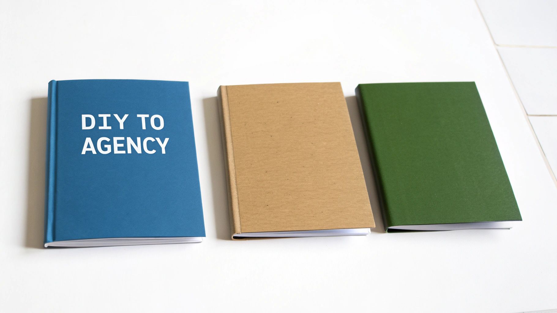 Three books on a white table: a blue book titled 'DIY TO AGENCY', a brown book, and a green book.
