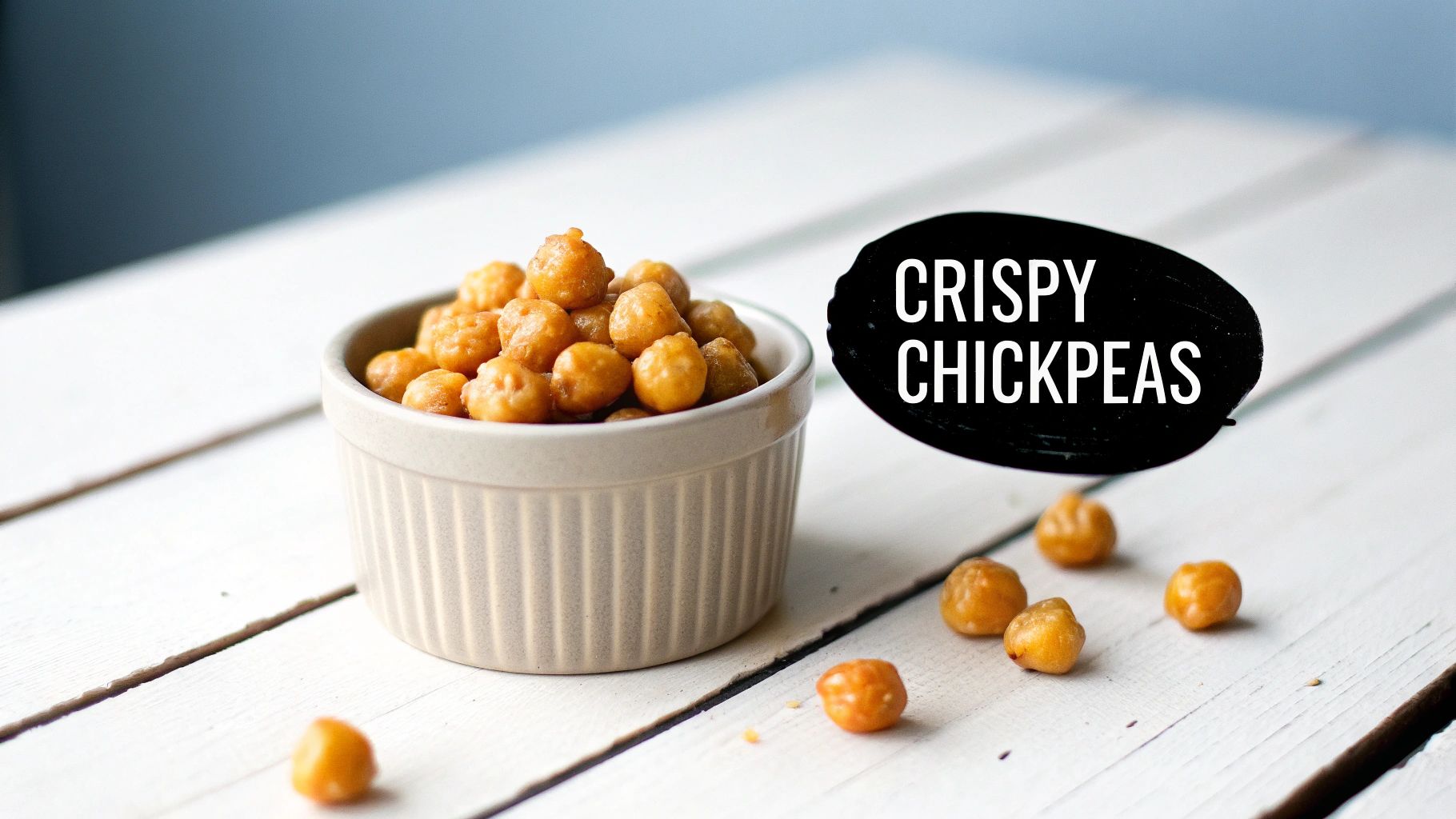 A ceramic bowl of golden crispy chickpeas on a white wooden table, with text 'CRISPY CHICKPEAS'.