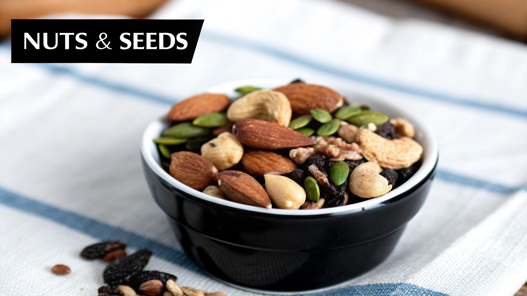 A black bowl filled with a colorful mix of almonds, cashews, hazelnuts, pumpkin seeds, and dried fruit.