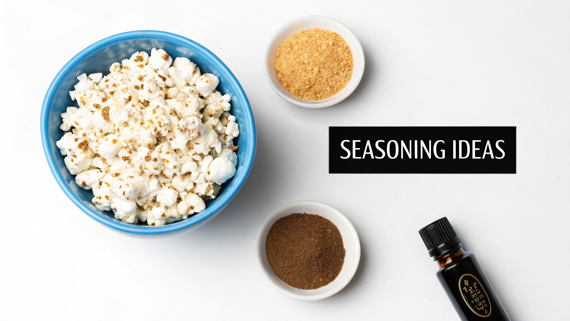 Seasoned popcorn in a blue bowl with two small bowls of spices and a dark liquid seasoning bottle.