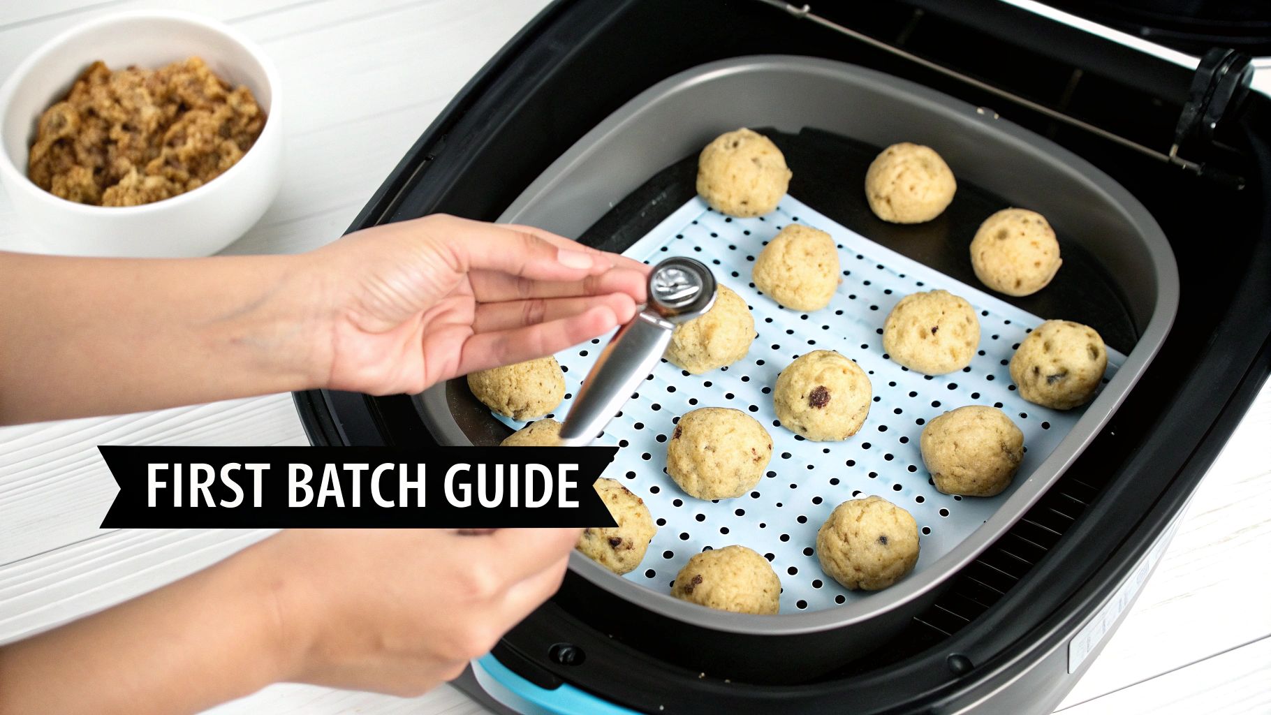 Hands place raw cookie dough balls onto a blue mat in an air fryer with a scoop.