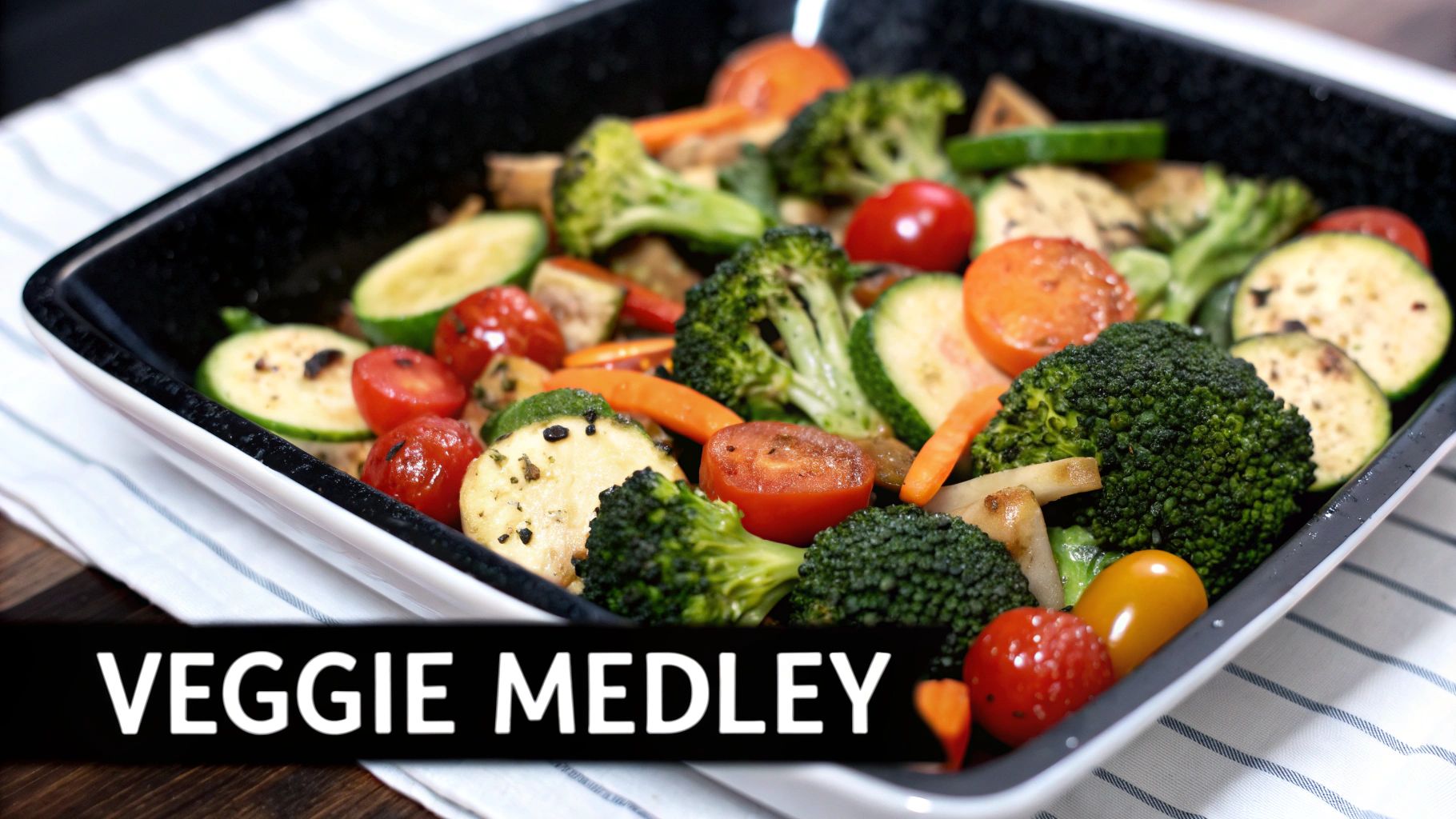 A black baking dish filled with a colorful medley of roasted broccoli, zucchini, carrots, and cherry tomatoes.