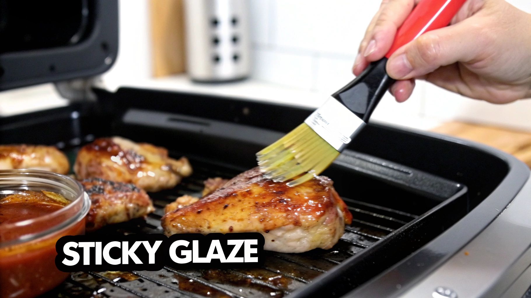 A hand brushes sticky glaze onto succulent chicken pieces cooking on an air fryer grill.