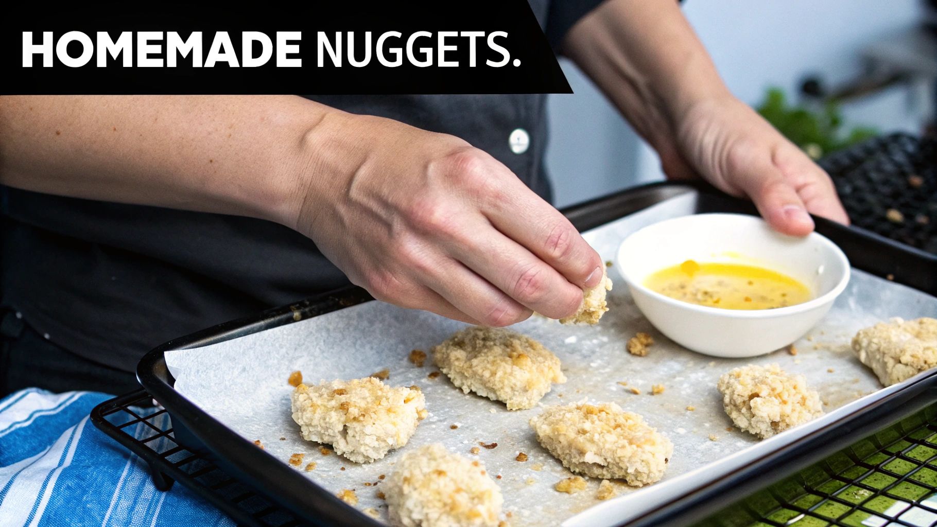 Close-up of hands preparing homemade breaded chicken nuggets on a baking sheet with a bowl of coating.