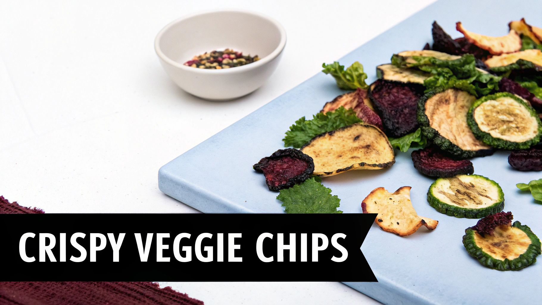 Assortment of colorful crispy veggie chips on a light blue cutting board with a bowl of spices.