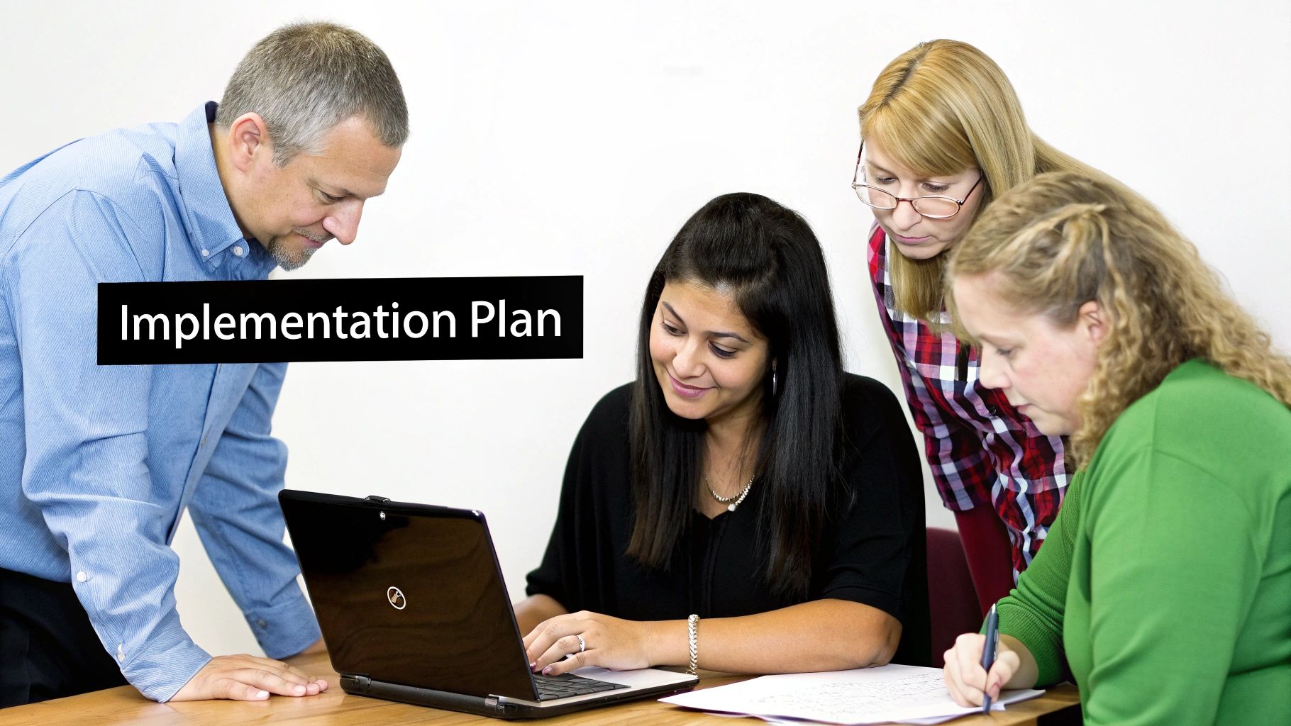 Four professionals, three women and one man, collaborating around a laptop and documents on an 'Implementation Plan'.