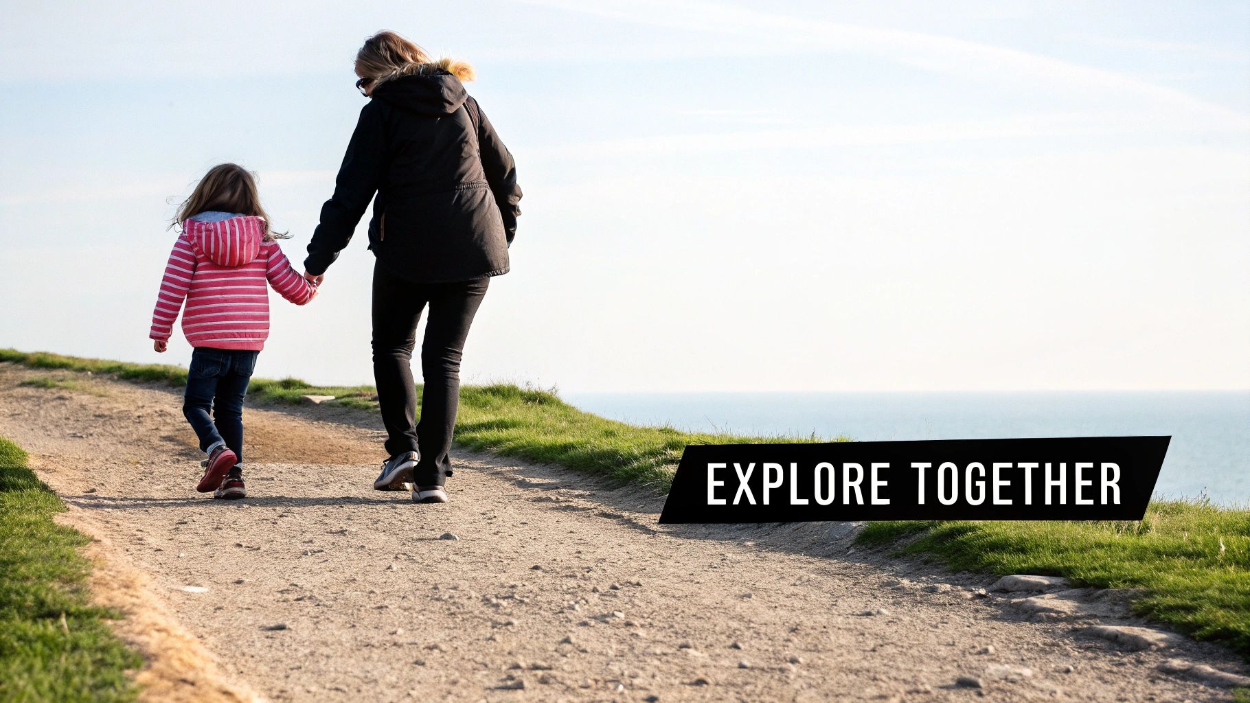 Mother and daughter holding hands walking together on coastal path with ocean view