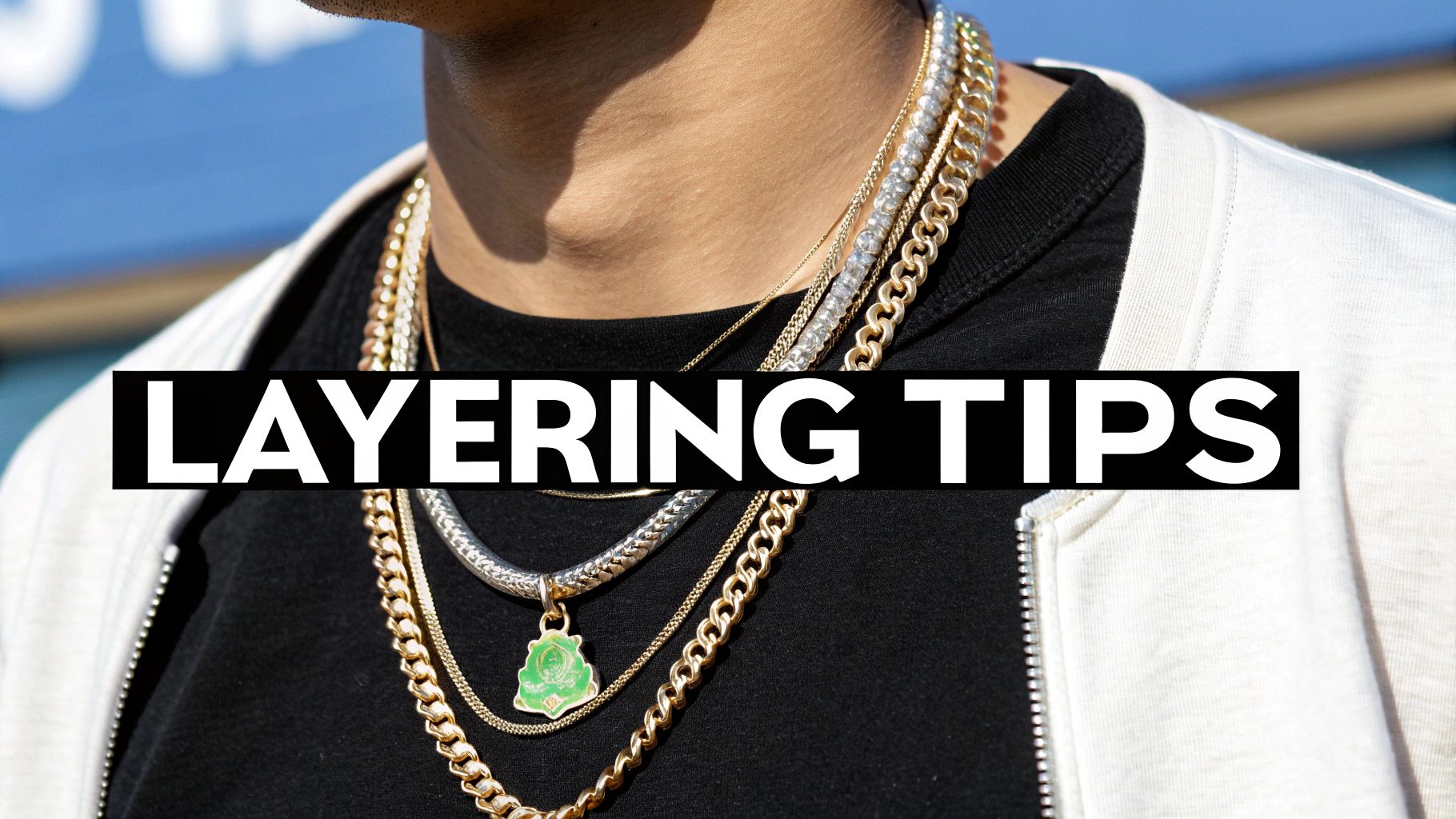 Close-up of a person wearing multiple layered gold and silver necklaces with a green pendant over a black shirt.