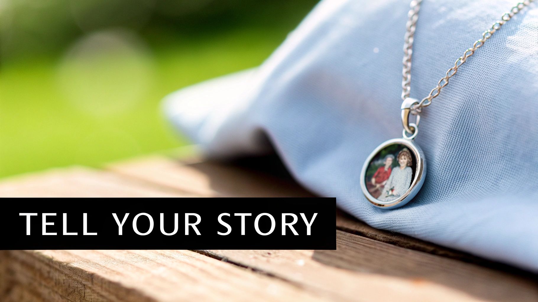 A silver locket necklace with a photo of two women, resting on light blue fabric and wood.
