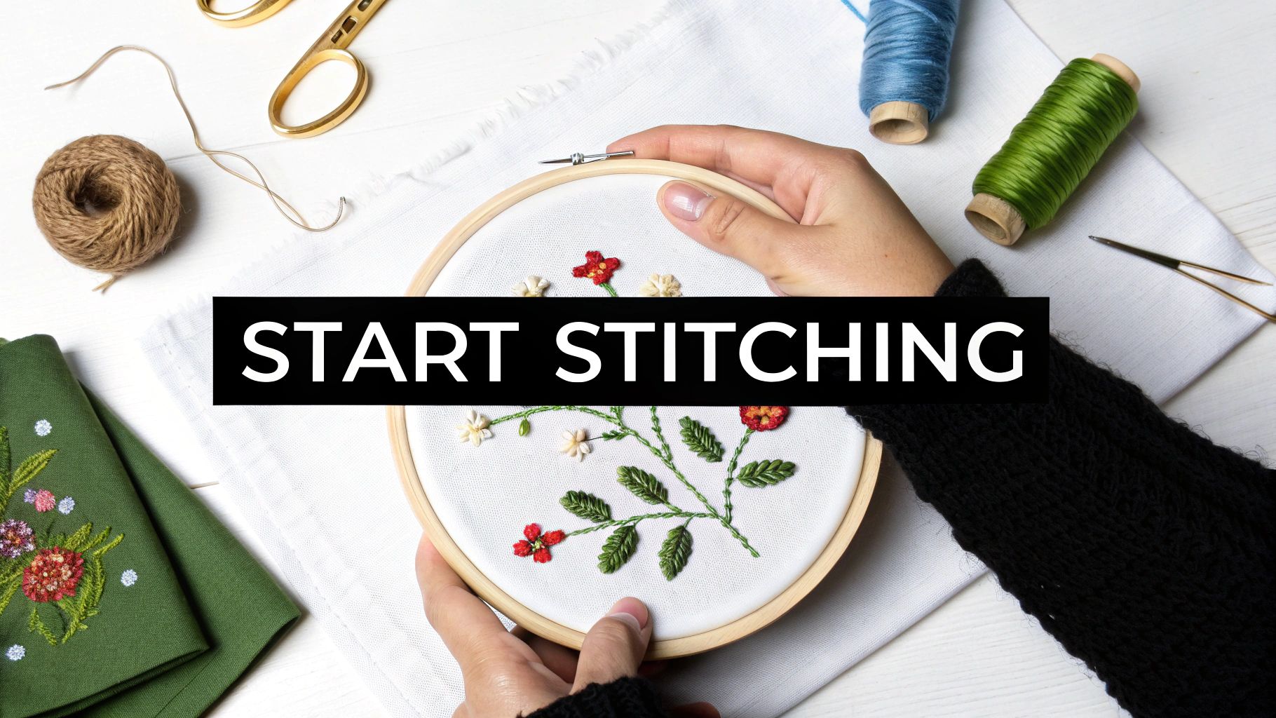 Overhead view of hands holding an embroidery hoop with a floral pattern, surrounded by stitching supplies.