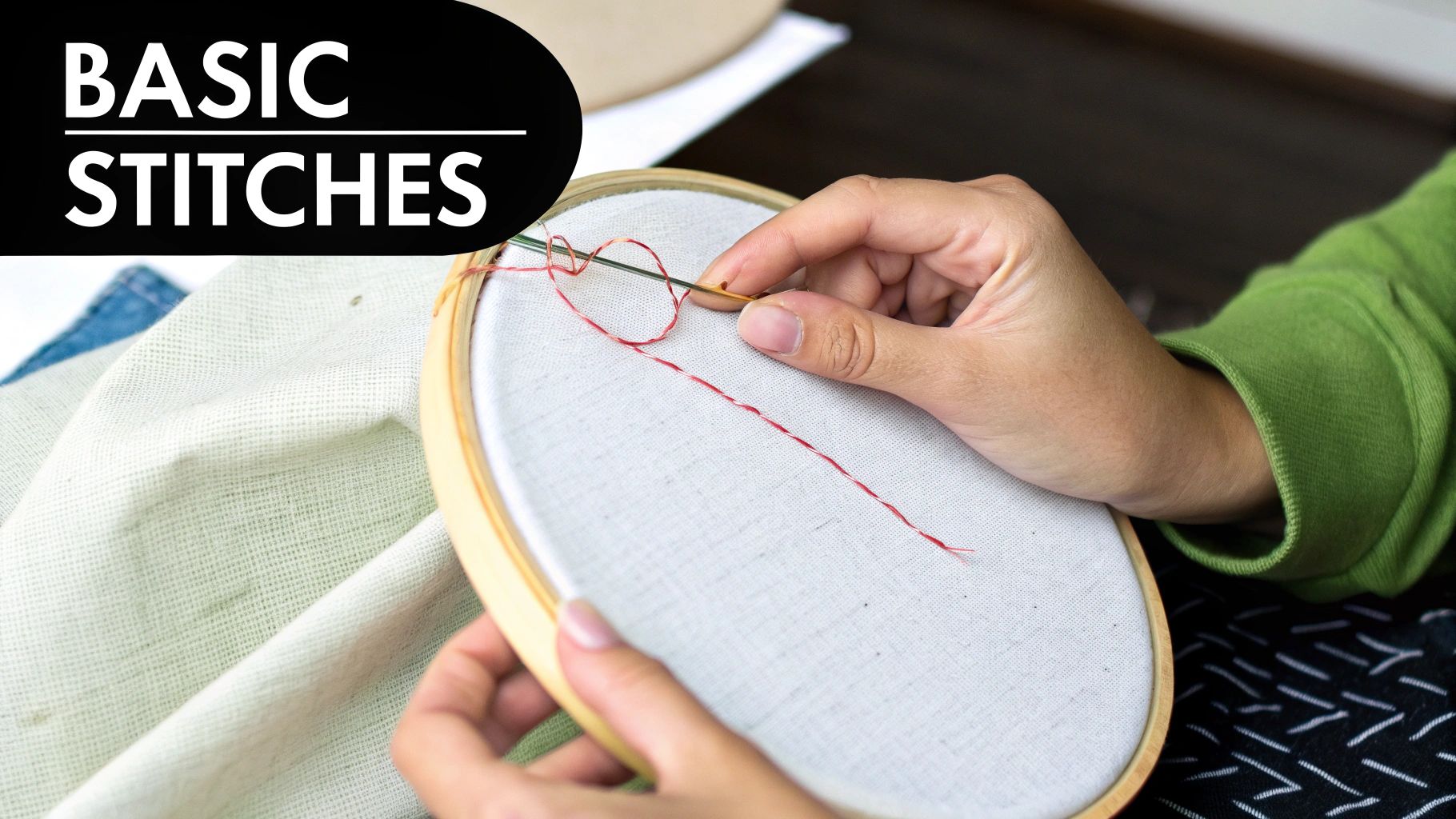 Hands demonstrating a basic embroidery stitch with red thread on white fabric in a wooden hoop.