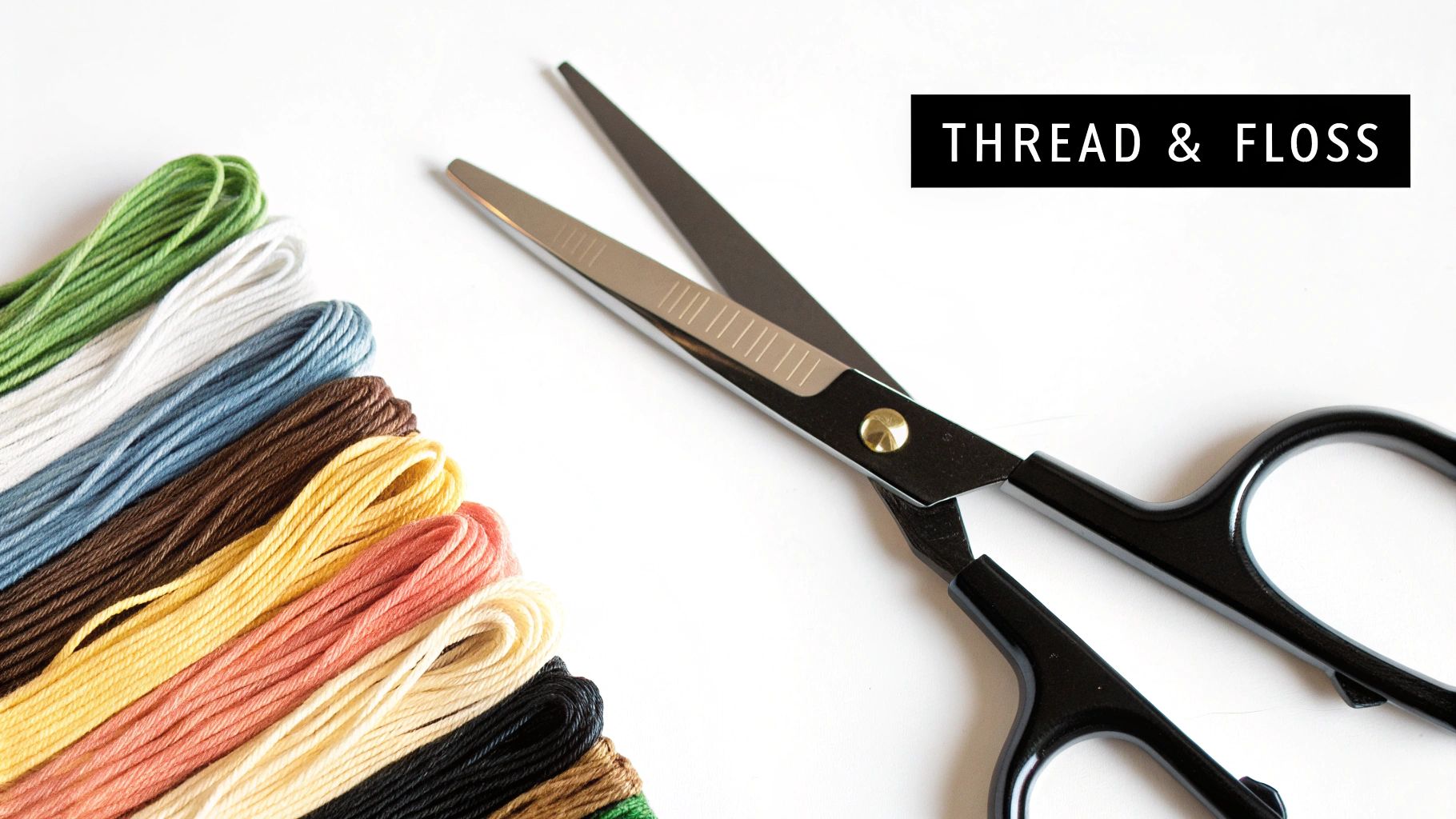 Colorful embroidery floss bundles in various shades next to black-handled scissors on a white surface.