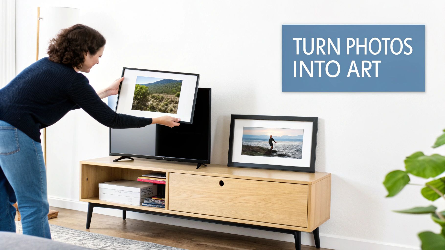 A woman placing a framed landscape photo above a television, creating art from memories.