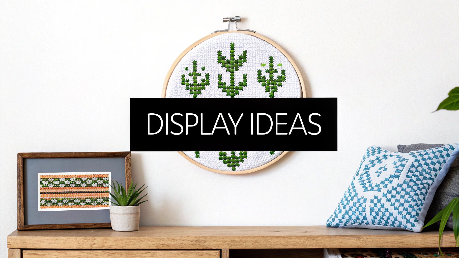 Crafted cross-stitch art, including framed and hoop designs, displayed on a wooden shelf with plants.