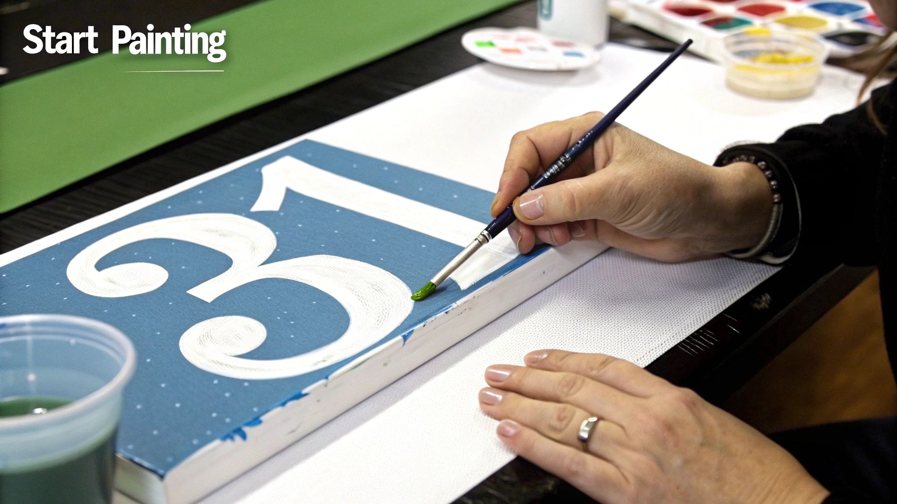 Close-up of a person painting white numbers '31' on a blue canvas with a brush and green paint.