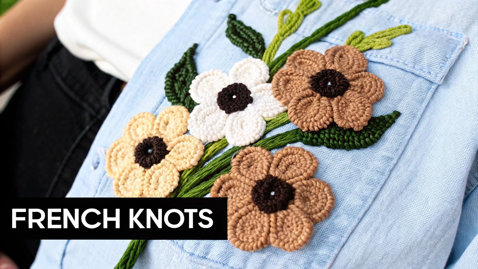 Close-up of a light blue denim shirt featuring French knot floral embroidery in white, brown, and green.