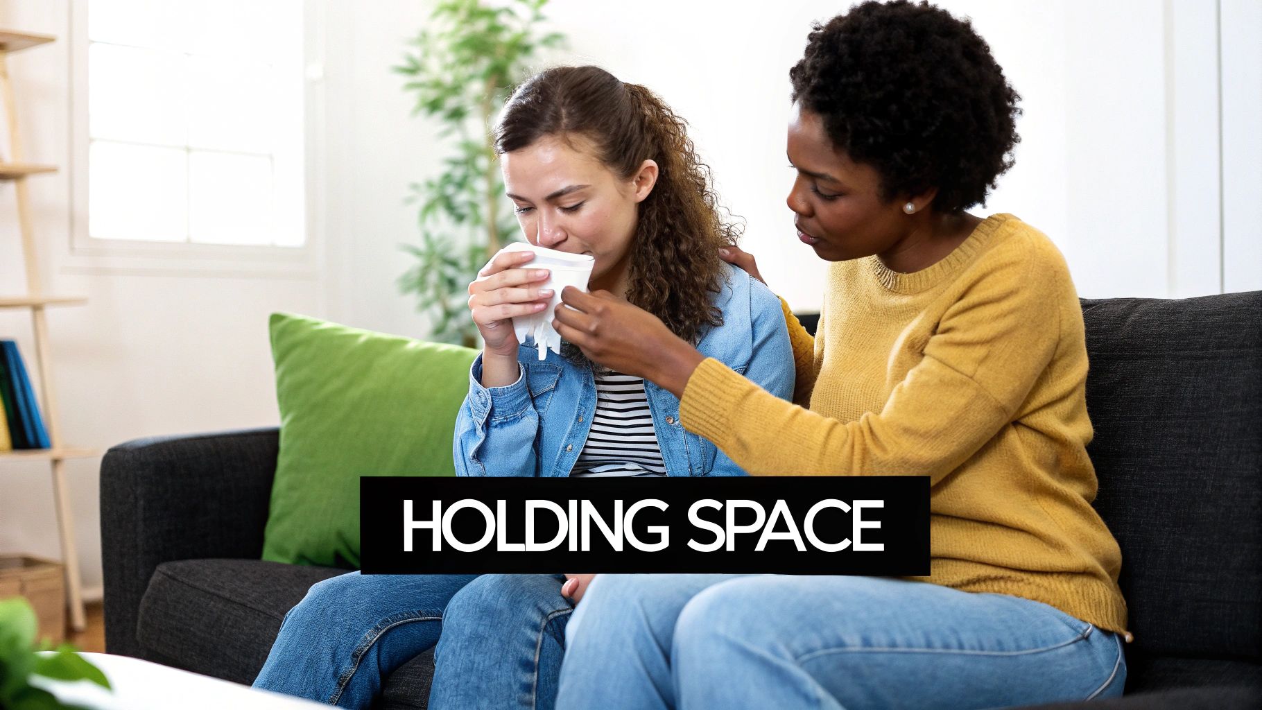 A supportive woman comforts a distressed woman holding a tissue, sitting together on a couch.