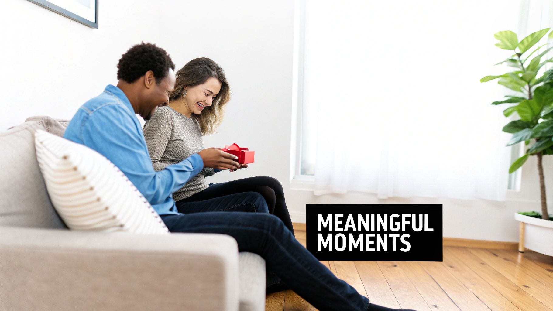 A happy couple on a sofa, the man presenting a red gift box to the smiling woman.