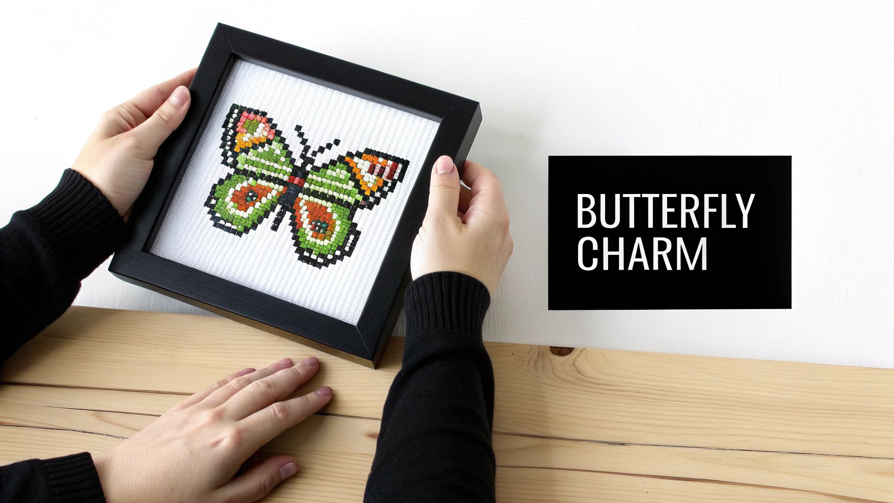 Hands hold a framed, colorful butterfly cross-stitch artwork, with 'BUTTERFLY CHARM' text on a white background.