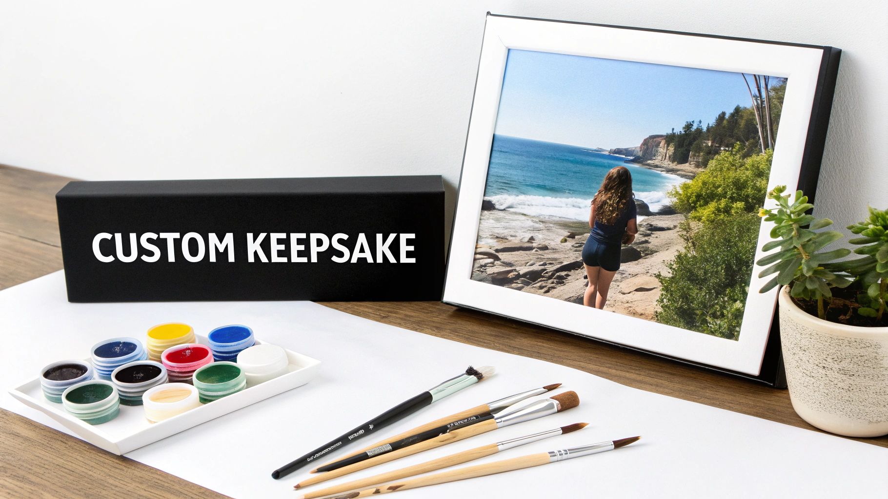 A custom keepsake box, framed photo of a scenic beach, paint set with brushes, and a succulent plant.