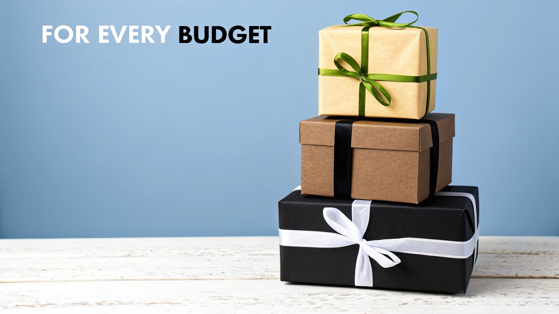 Three stacked gift boxes in brown, black, and kraft paper with colorful ribbons, on a white wooden table.