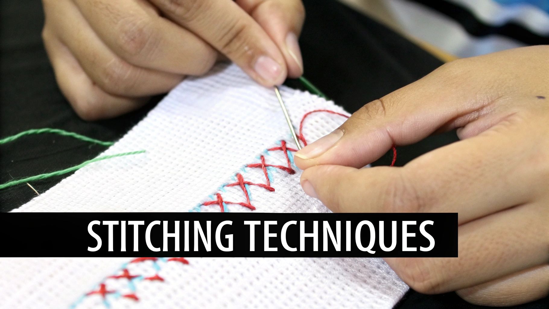 Close-up of hands cross-stitching colorful patterns with a needle and red thread on white fabric.