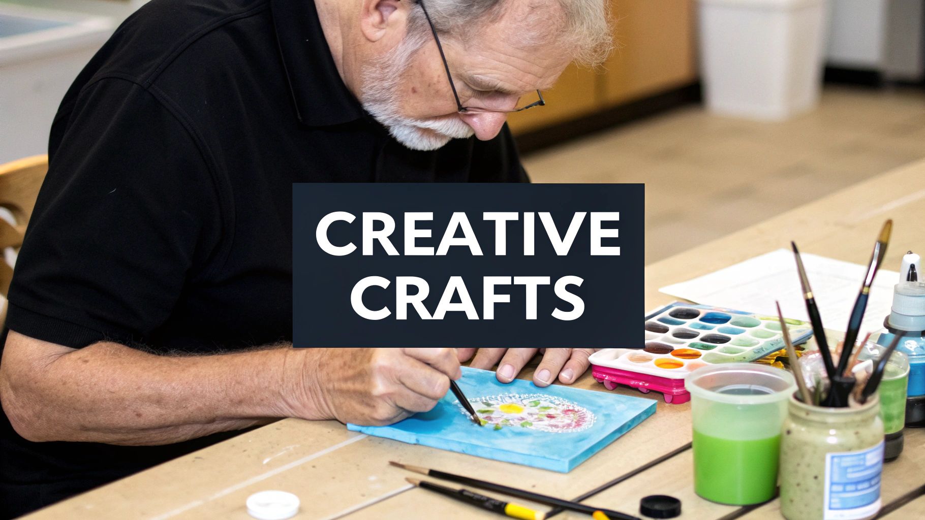 Senior man engaged in creative painting craft activity using watercolors and brushes at wooden table