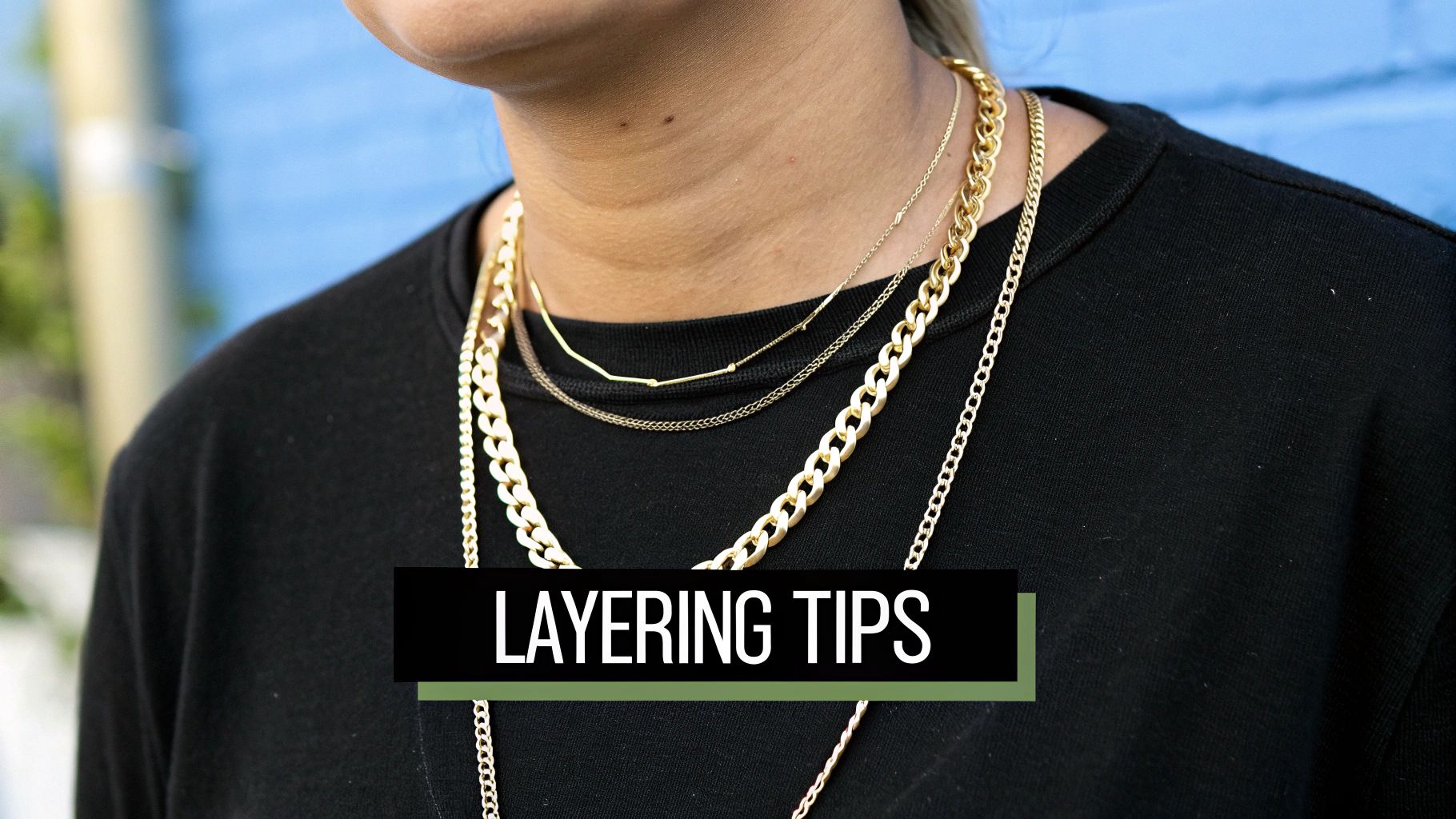 Close-up of a person wearing multiple stylish gold layered necklaces over a black top, showcasing fashion tips.