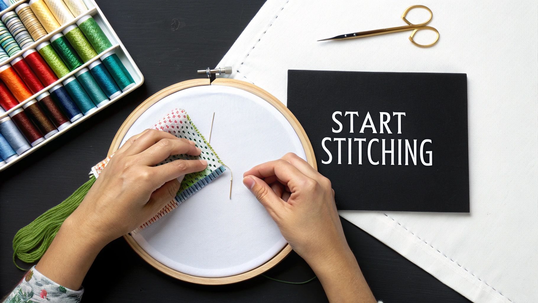Overhead view of hands cross-stitching on fabric in an embroidery hoop, surrounded by threads and scissors.