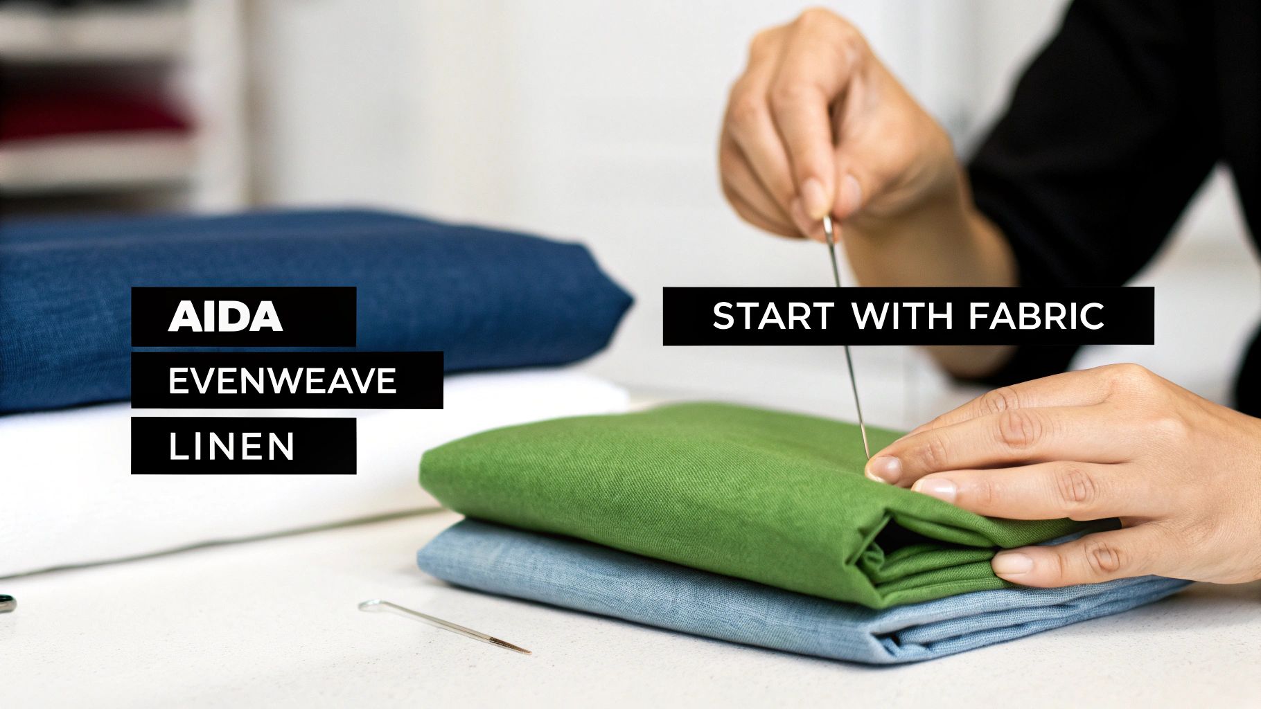 Hands hold a needle over folded Aida, Evenweave, and linen fabrics for cross-stitch.