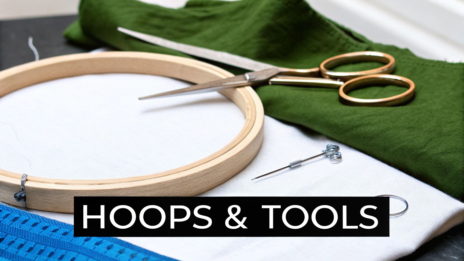 Embroidery hoop with white fabric, scissors, needle, and green cloth showing essential cross stitch supplies