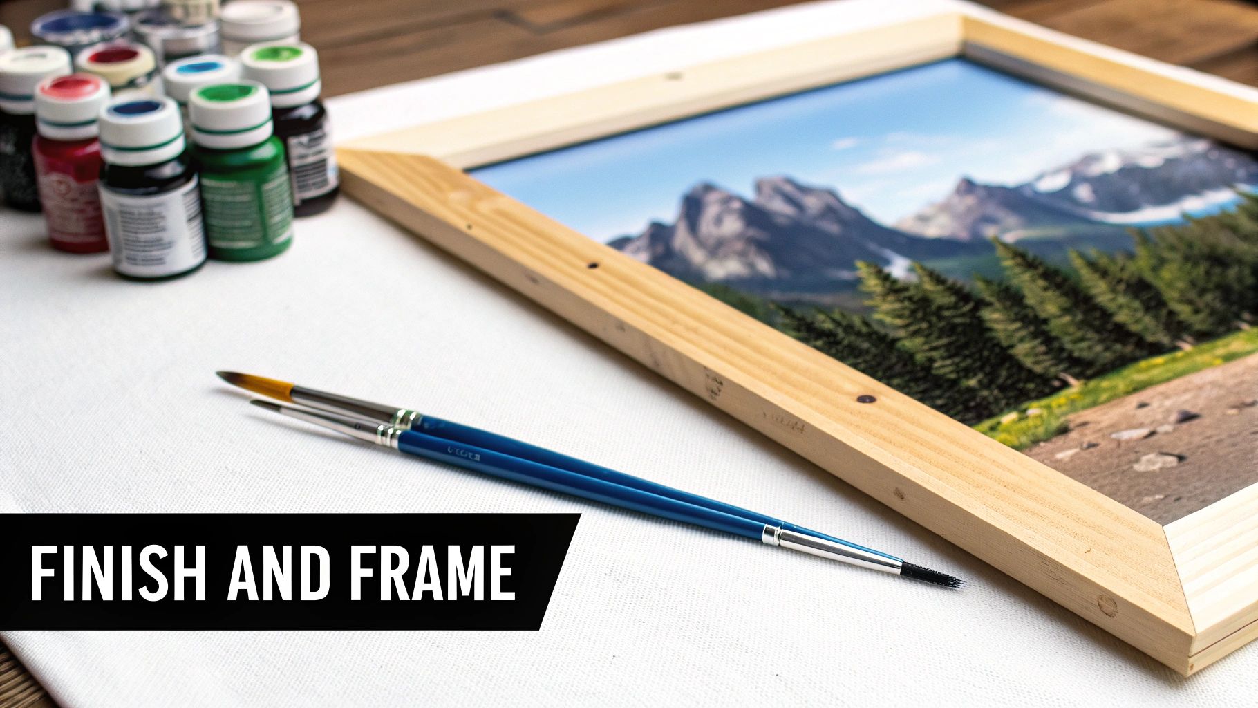 Paints, brushes, and a framed landscape painting with text 'FINISH AND FRAME' on canvas.