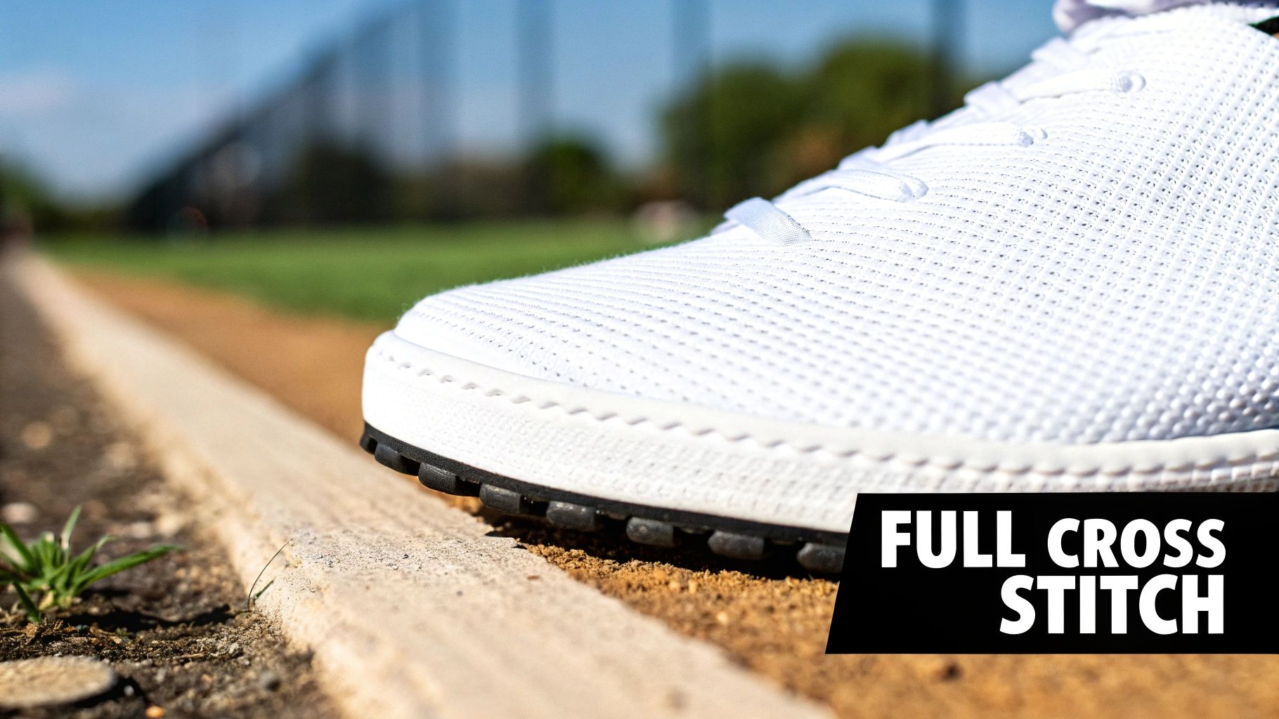 Close-up of a white shoe with 'FULL CROSS STITCH' texture on a dirt path next to a curb.