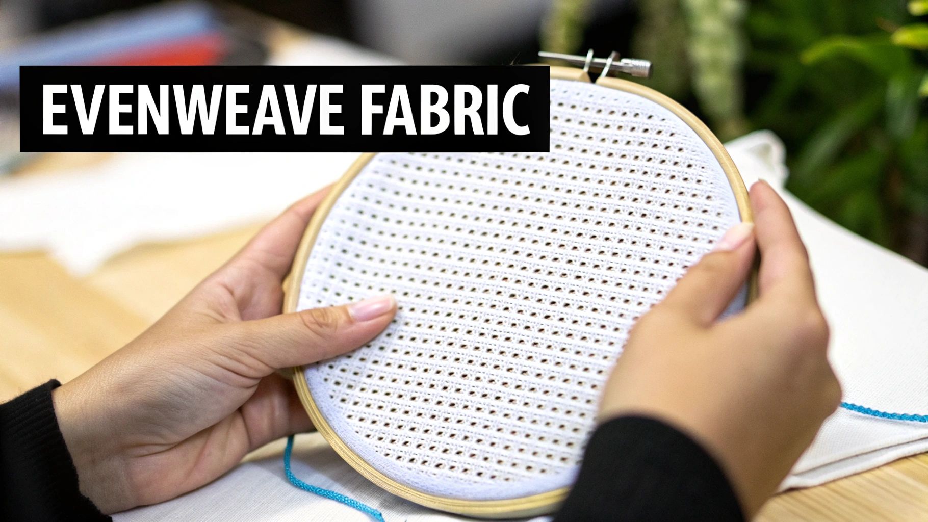 Close-up of hands holding white evenweave fabric stretched in a wooden embroidery hoop for crafting.