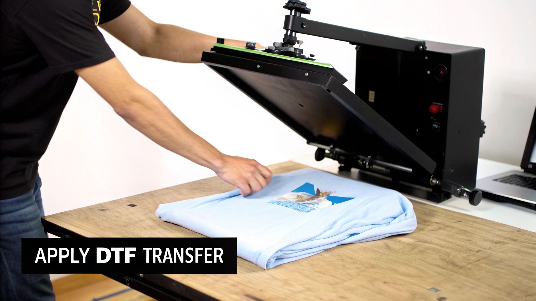 A person prepares a light blue t-shirt with a graphic for DTF transfer on a heat press.