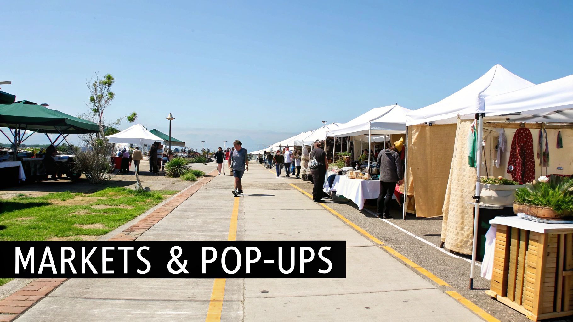 Outdoor waterfront market with white tents, vendors, and shoppers browsing handmade goods and crafts