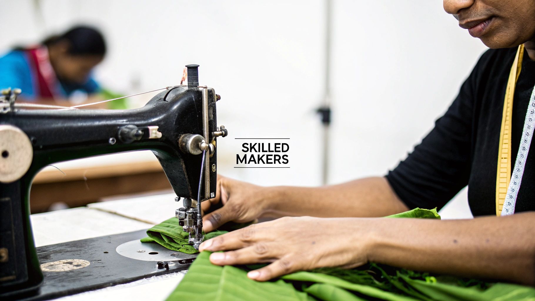 A skilled worker operates an old sewing machine, stitching green fabric in a busy workshop.