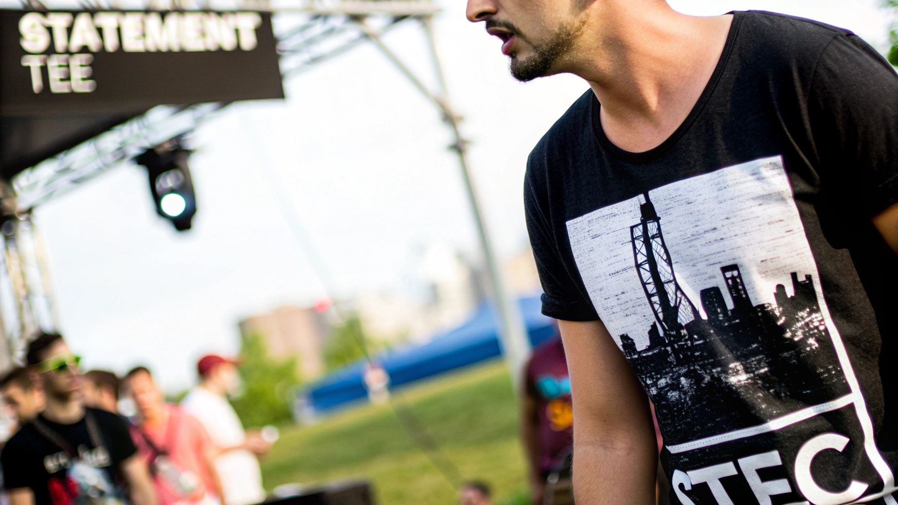 Close-up of a man wearing a black t-shirt with a city skyline graphic at an outdoor music festival.