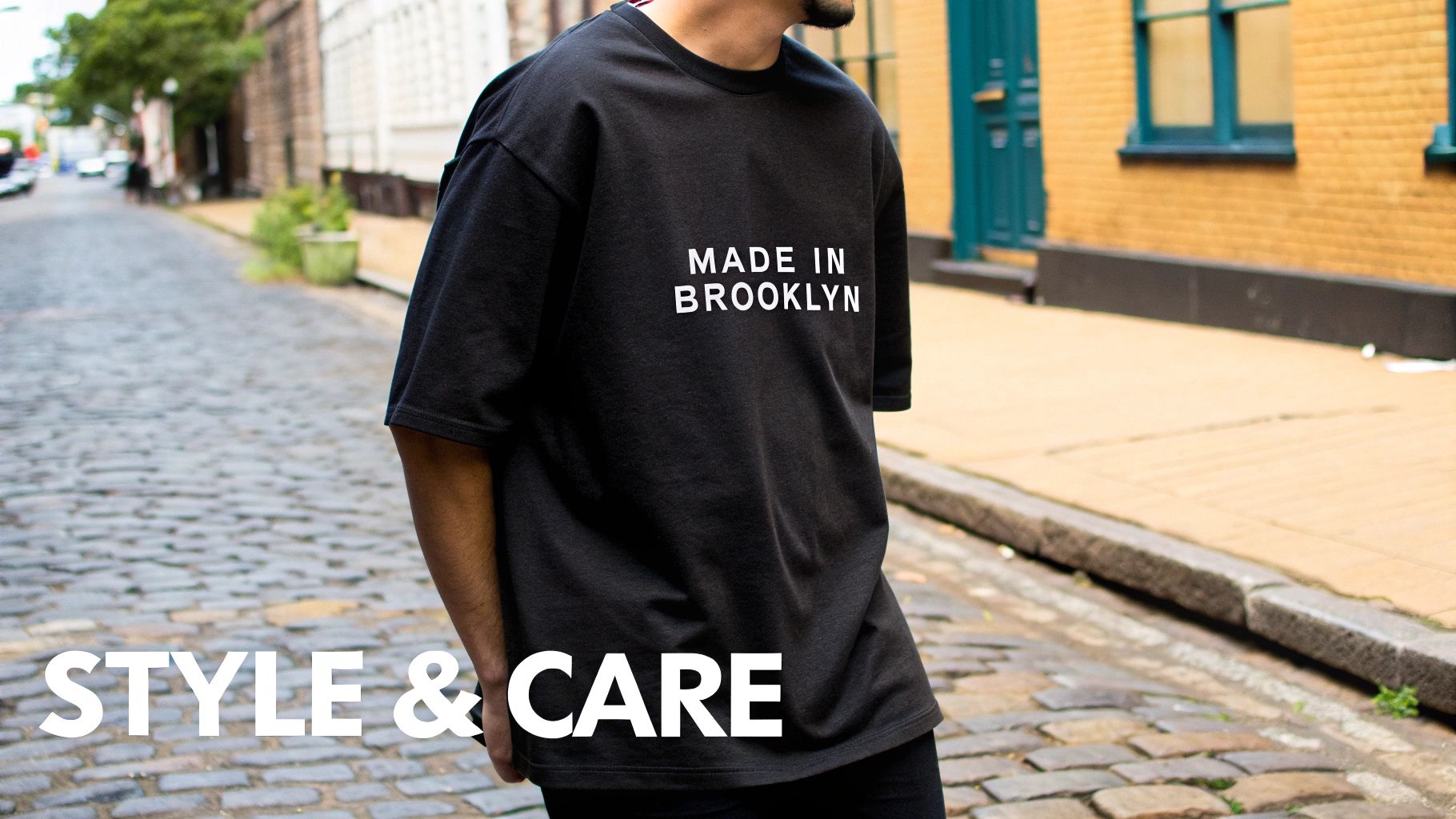 A person wearing a black oversized t-shirt with “MADE IN BROOKLYN” text on a cobblestone street.