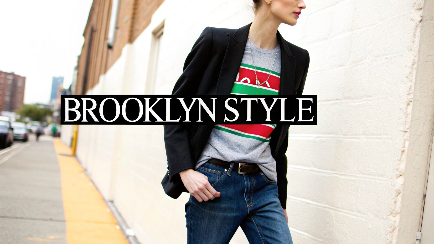 A stylish person in a black blazer, grey striped tee, and jeans walking down a Brooklyn street.