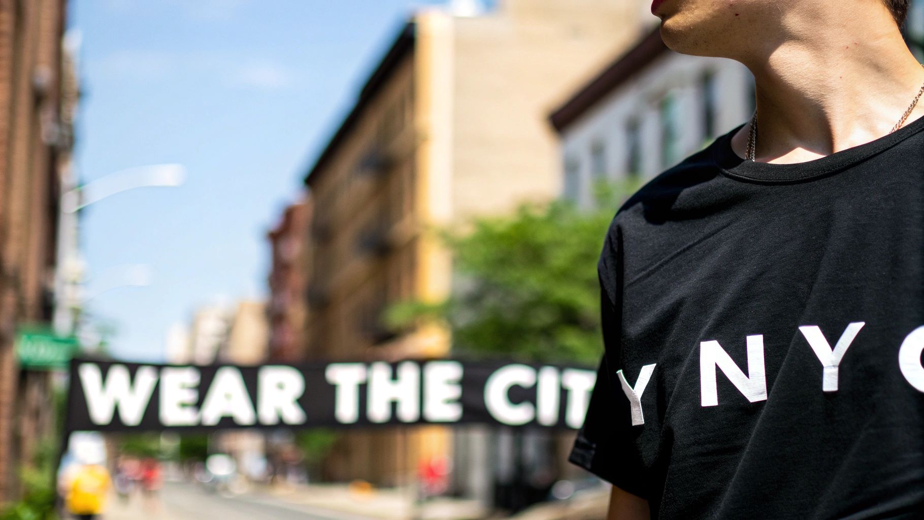 A person wears a black t-shirt with "NYC" text, blurred city street and a banner in the background.