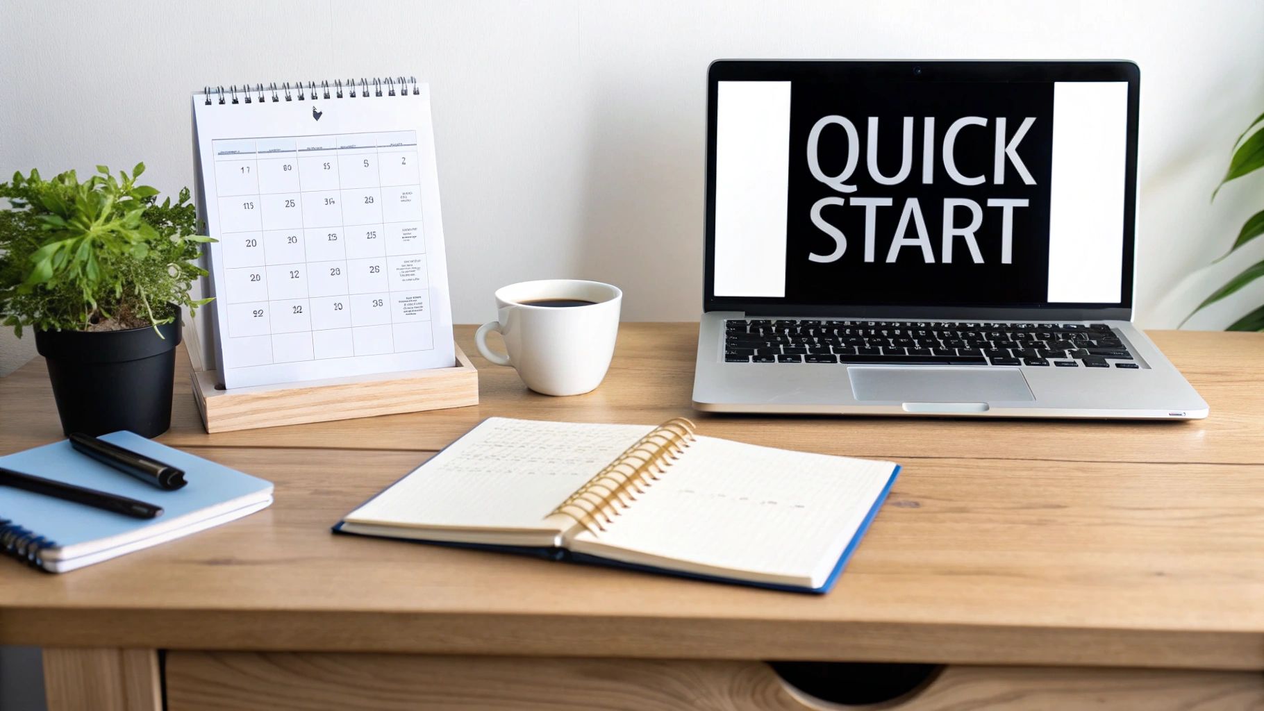 A clean wooden desk with a laptop showing 'QUICK START', calendar, coffee, and notebooks.