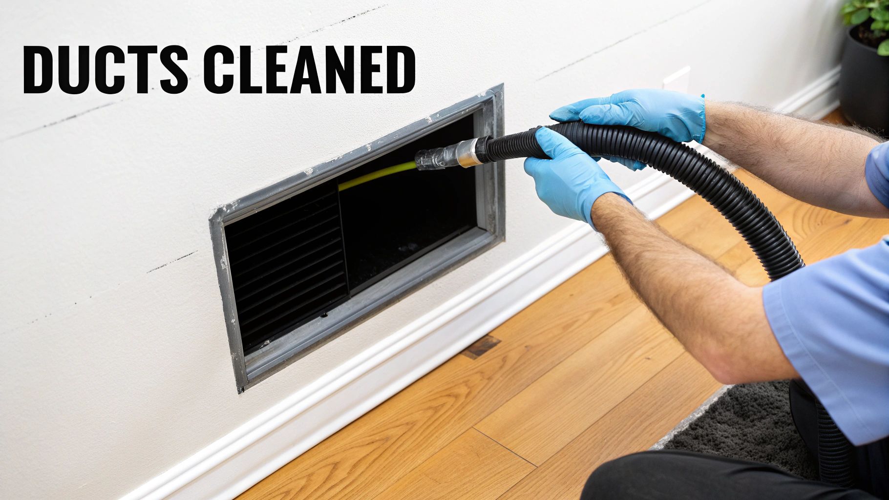 A professional in blue gloves is cleaning an air duct vent on a white wall with a hose.
