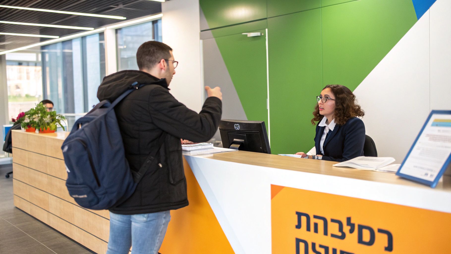 גבר משוחח עם פקידת קבלה בדלפק מודרני, עם קירות צבעוניים ברקע.