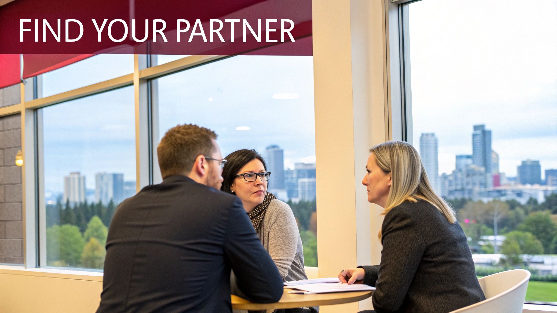 Three professionals discussing at a table with a city skyline in the background, near a window.